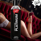 A large bottle of Wet Platinum Premium Silicone Lubricant is prominently displayed in the foreground, offering a promise of a long-lasting experience. In the background, someone dressed in red high heels and lingerie relaxes on an ornate sofa. The vintage setting evokes an ambiance ideal for indulgence, even during steamy shower encounters.
